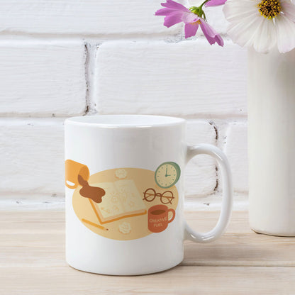 White ceramic mug featuring a playful late-night creativity illustration with coffee, notebooks, and a clock, shown in a styled product mockup with flowers and a white brick background for wid Designs.