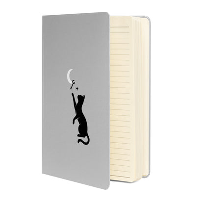 Curious Things hardcover lined notebook opened to show cream-colored pages and the cat and moon on silver cover design.